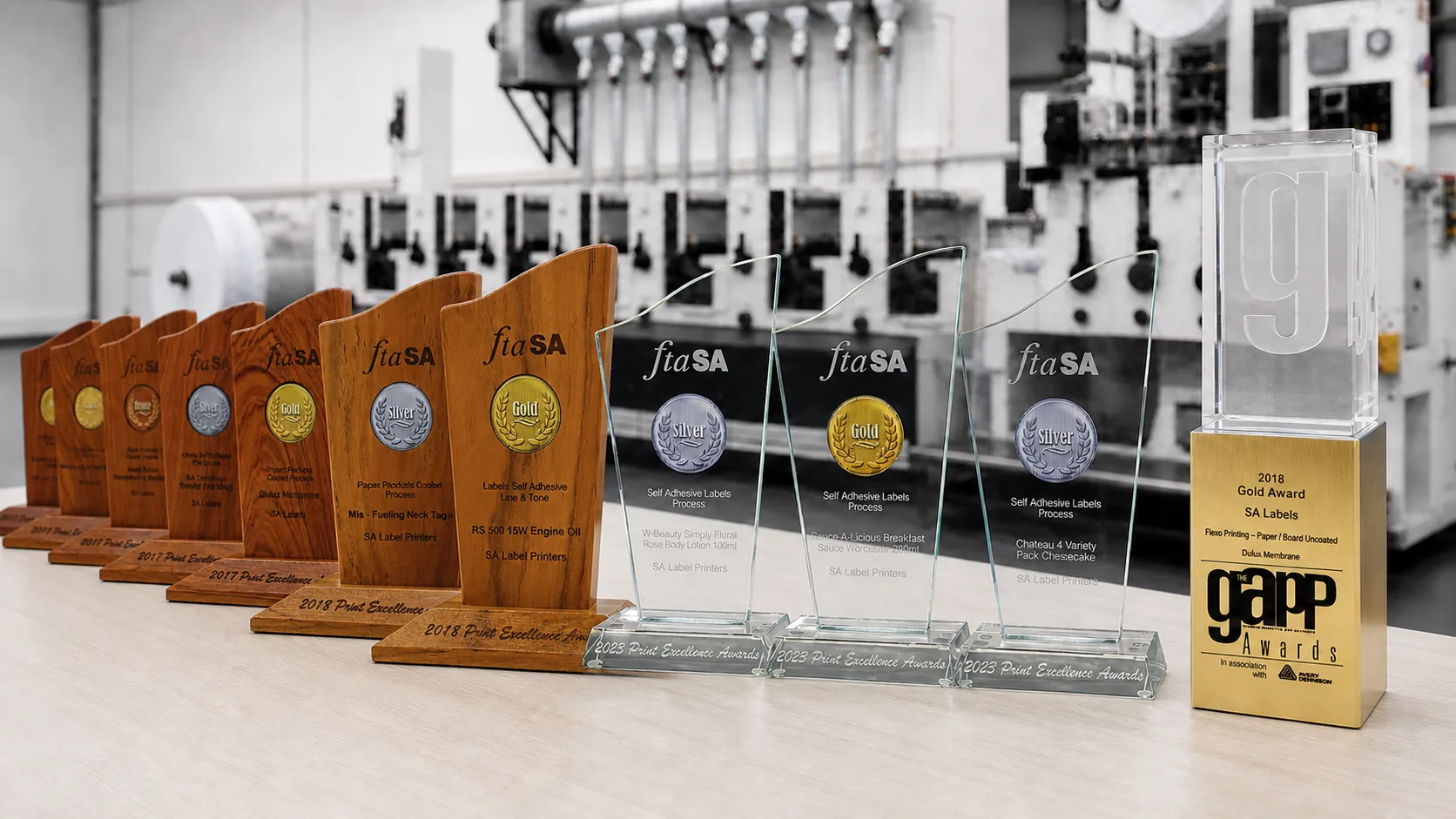 FTASA Print Excellence trophies and the 2018 GAPP gold award lined up on a bench in front of a flexographic press